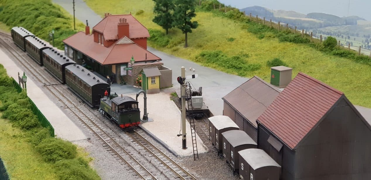A narrow gauge tank engine with a train of coaches at Blackmoor station, beside the goods shed