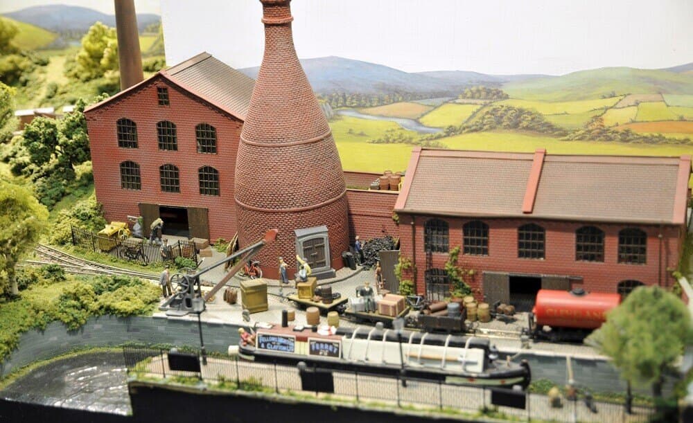 A pottery works with a bottle kiln beside a canal and railway