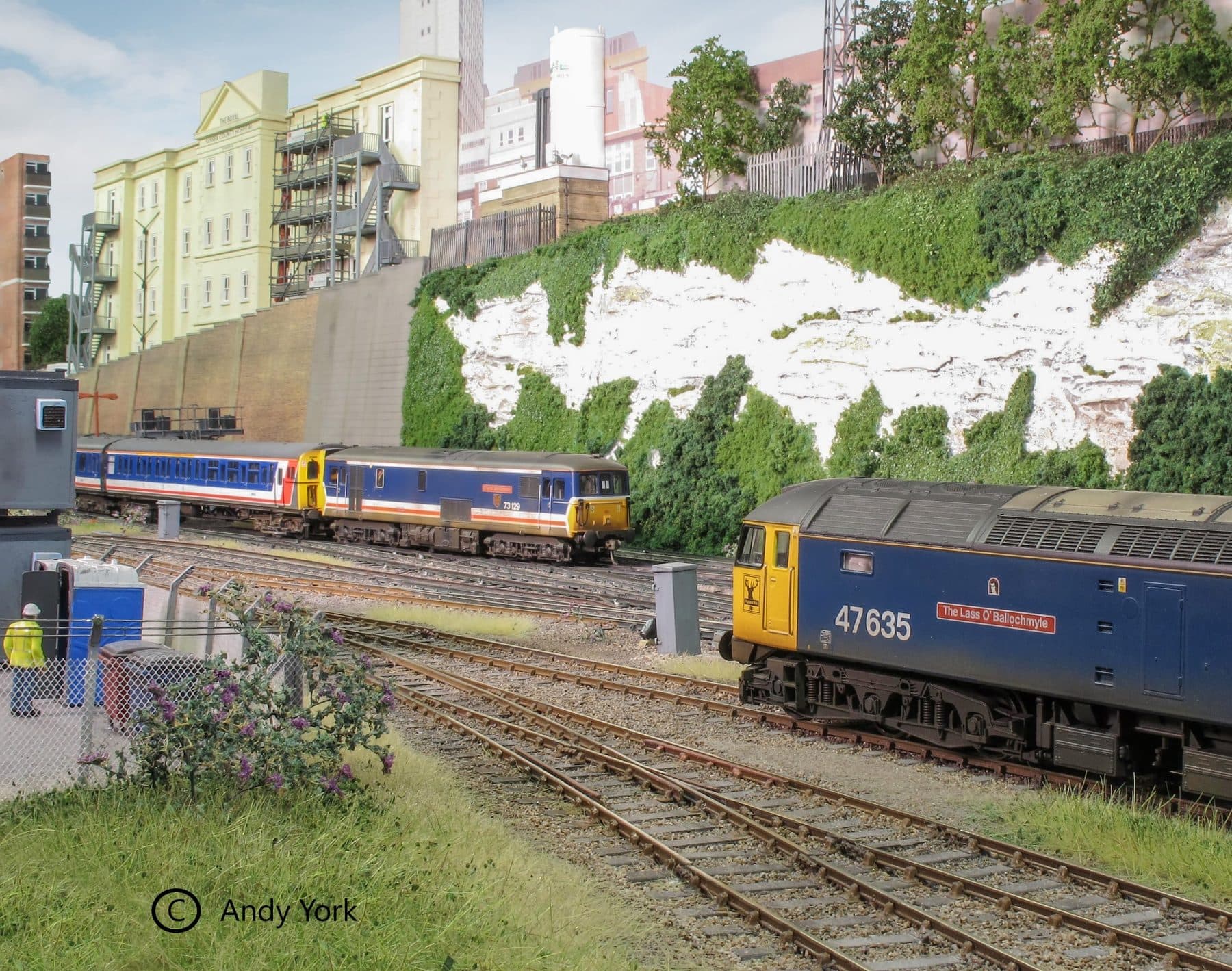 Network SouthEast electric units and a blue class 47 diesel beneath white chalk cliffs and modern flats