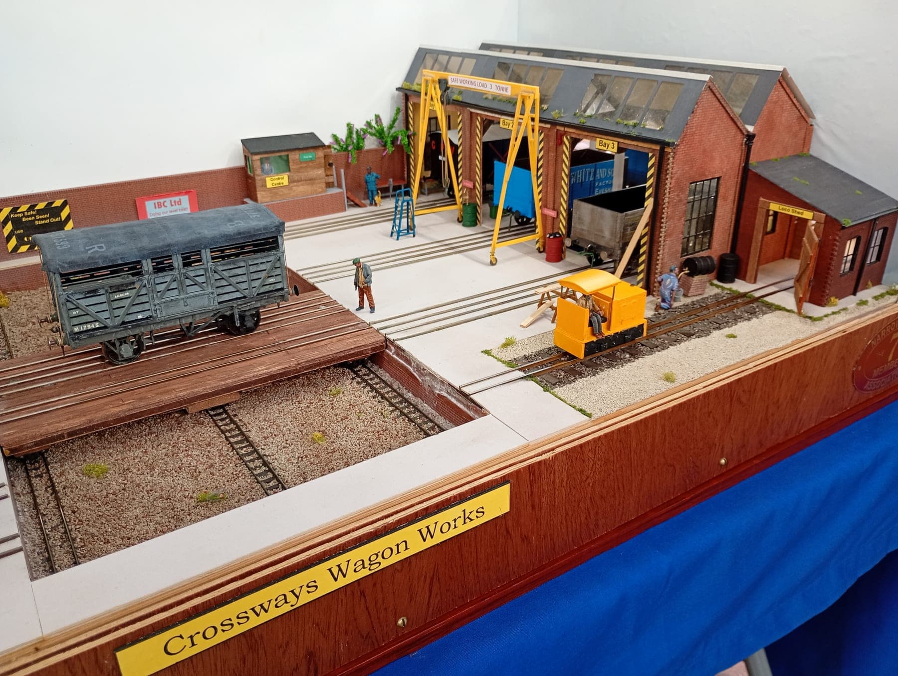 A yellow diesel shunter by the brick works sheds and gantry crane, with a grey goods van on the traverser
