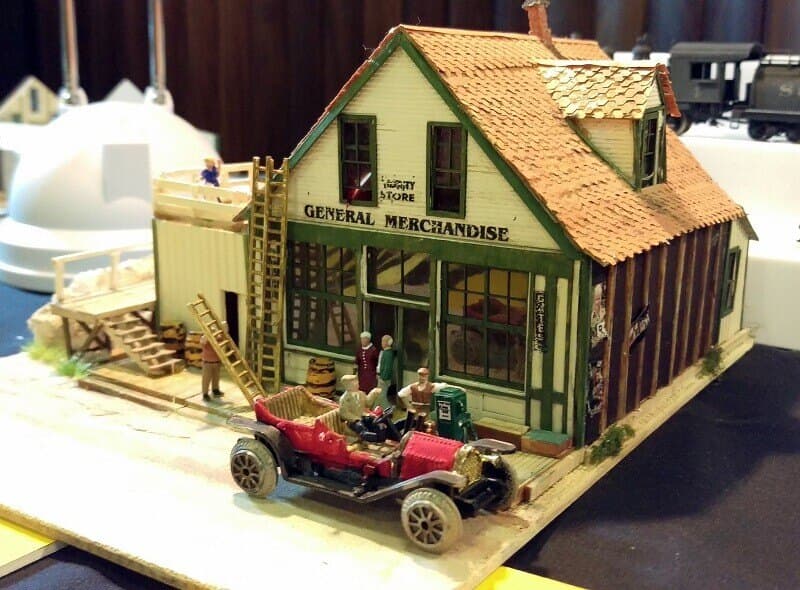 A narrow gauge general store with an old red car and figures outside