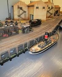 A steam tug in the creek beside the quay, with a locomotive on the wharf siding and warehouses behind
