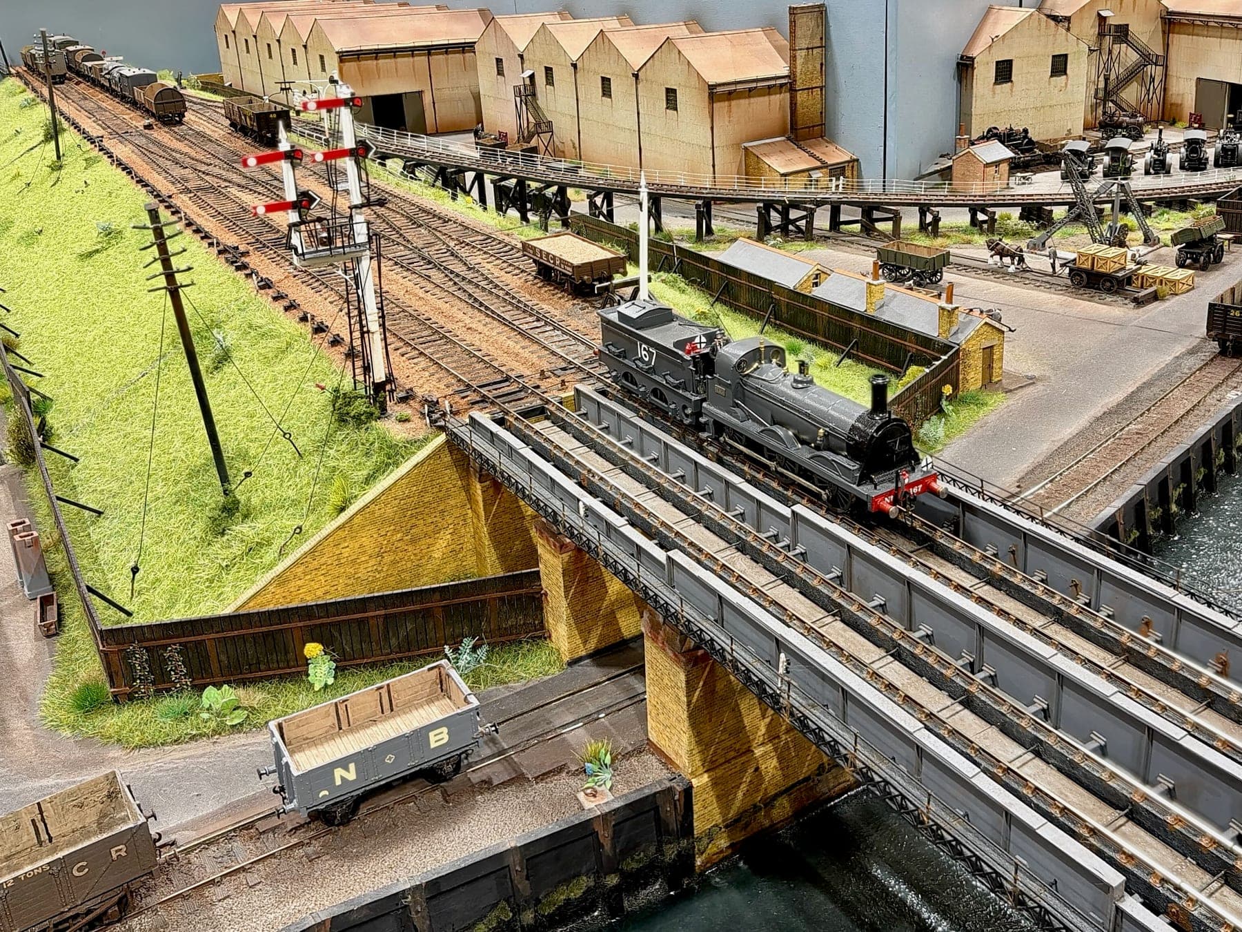 Engine 167 crosses the girder bridge over the creek, below the signals, with the warehouses and the wagons on the quay beyond