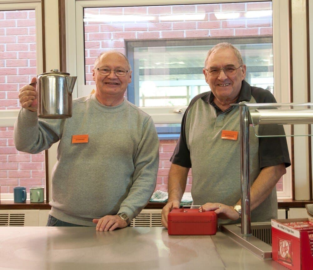 Two volunteers at the tea counter, one holding up a jug, at the 2016 show