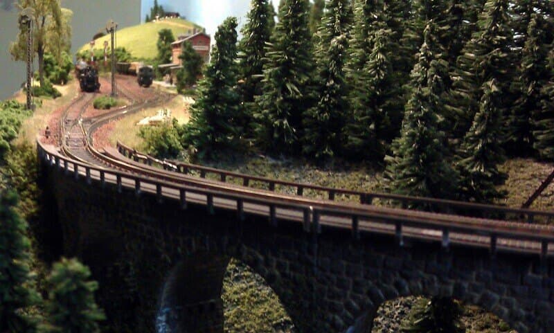 A stone viaduct curving through pine forest on a continental N gauge layout